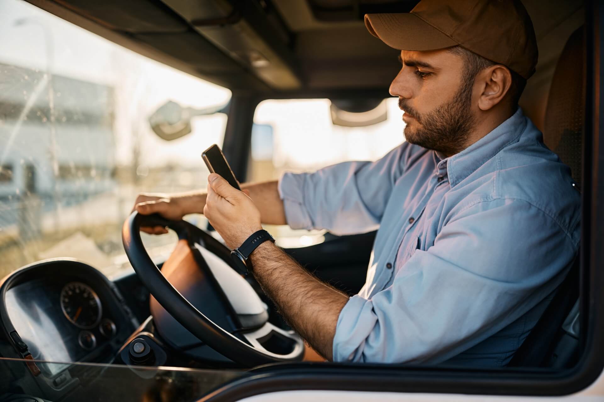 Trucker in a hat checking his phone behind the wheel.
