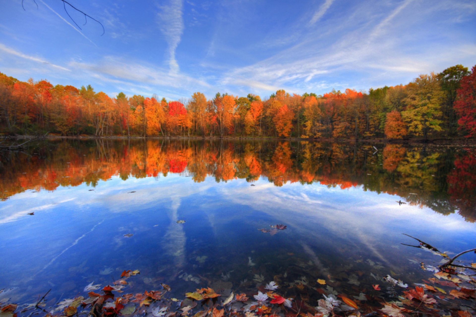 A water-level view of the Finger Lakes at autumn with the trees along the shoreline covered in orange, red and yellow leaves.
