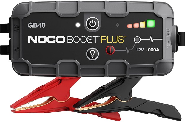 A NOCO Boost Plus external battery with built-in red and black jumper cables sits against a white background. It's an excellent tool for anyone learning how to use jumper cables because the built-in alligator clamps are easy to use and the battery is rechargeable.