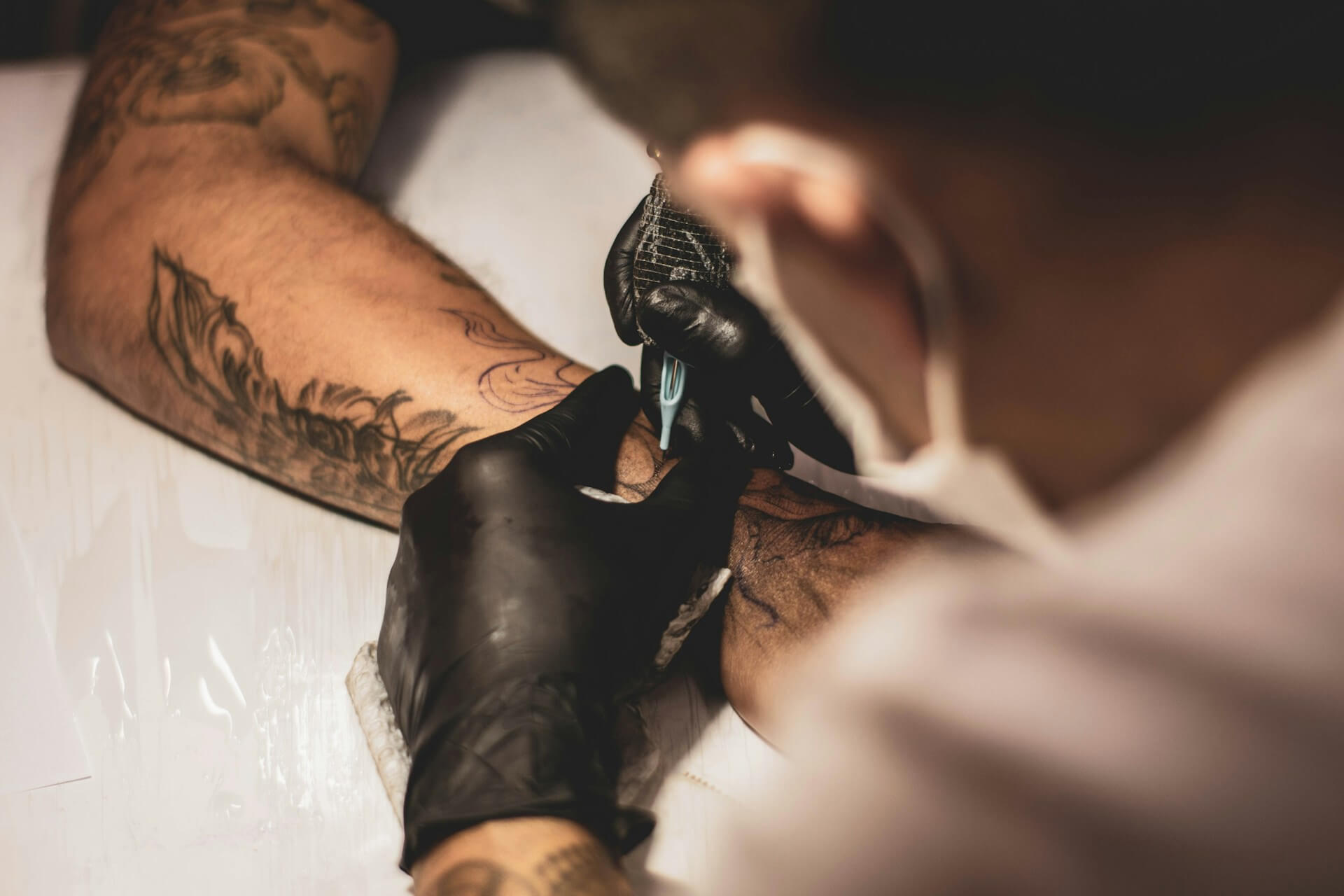 A person gets a tattoo filled in by a professional tattoo artist. They use a similar gun to stick and poke tattoo guns while wearing black latex gloves.