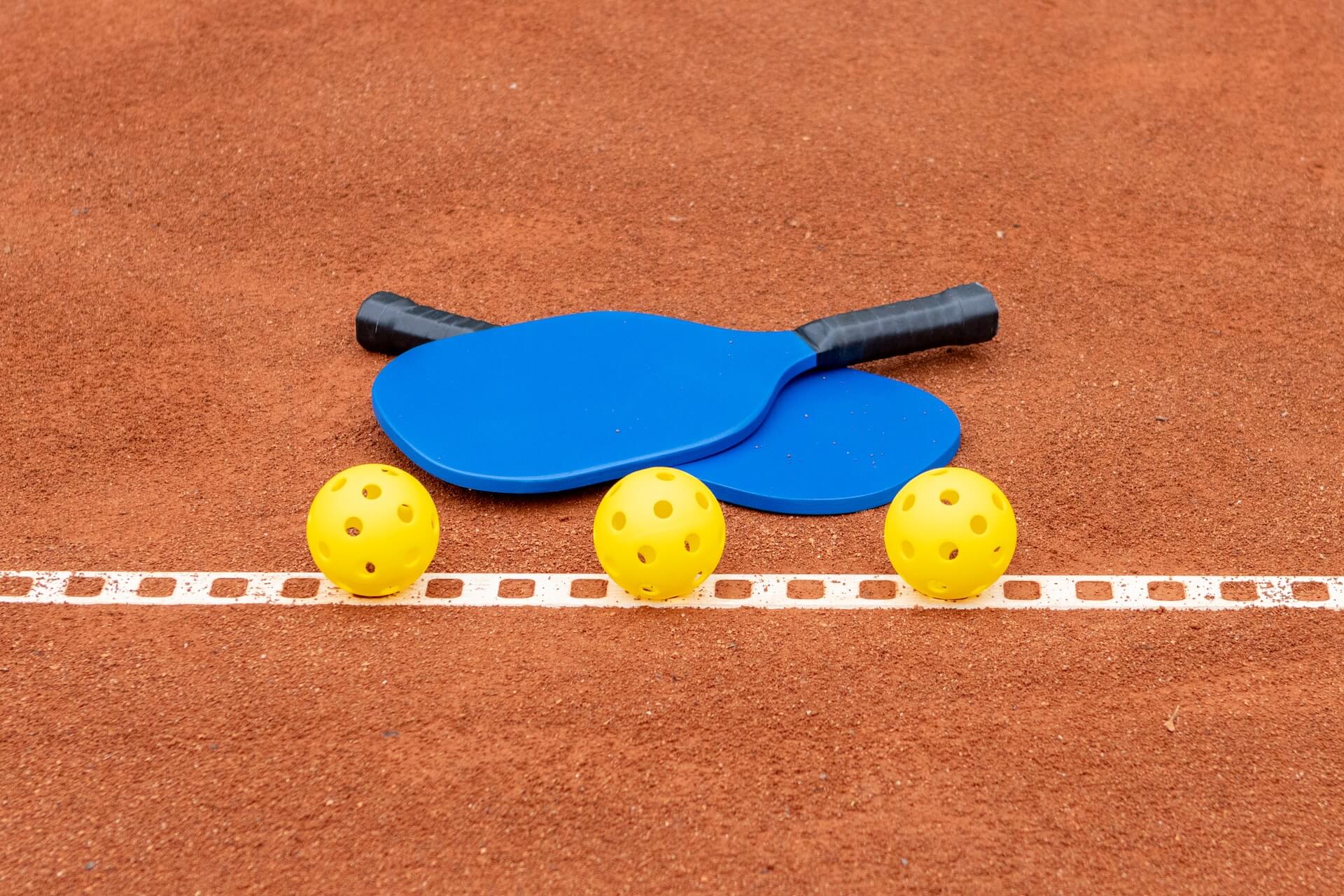 Two pickleball paddles and three balls lie on the court.