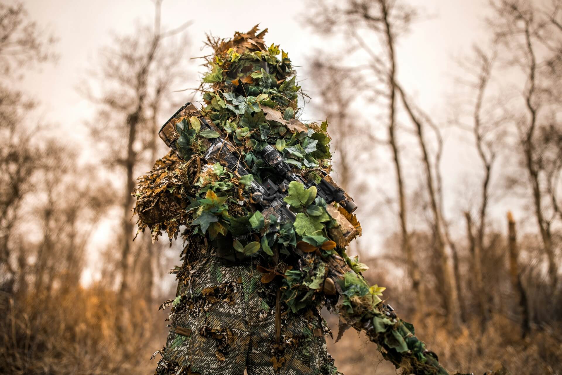 A sniper in a ghillie suit standing in the woods.