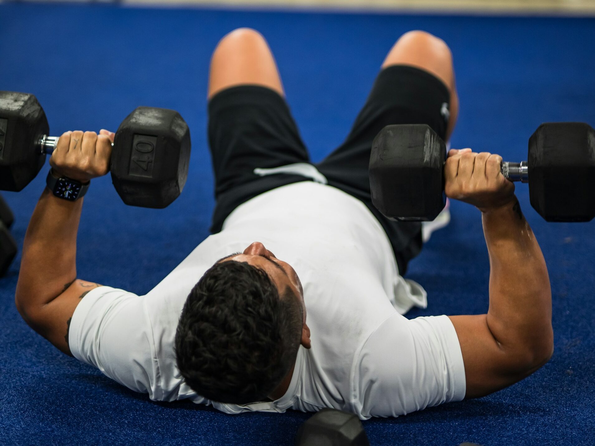 A man in a white shirt lifting dumbbells on the floor.