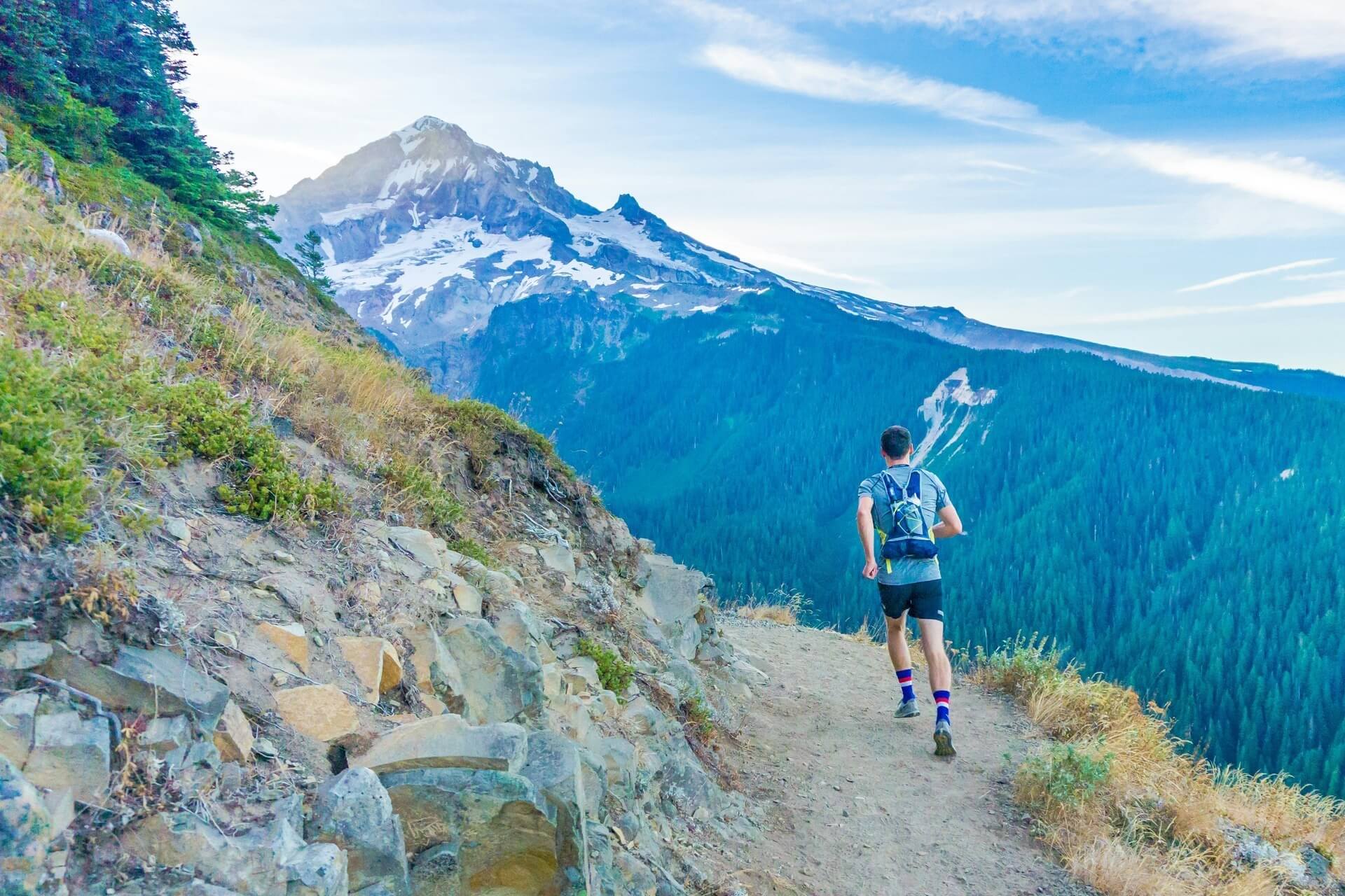 A fastpacking enthusiast jogging on a trail along the edge of a mountain.
