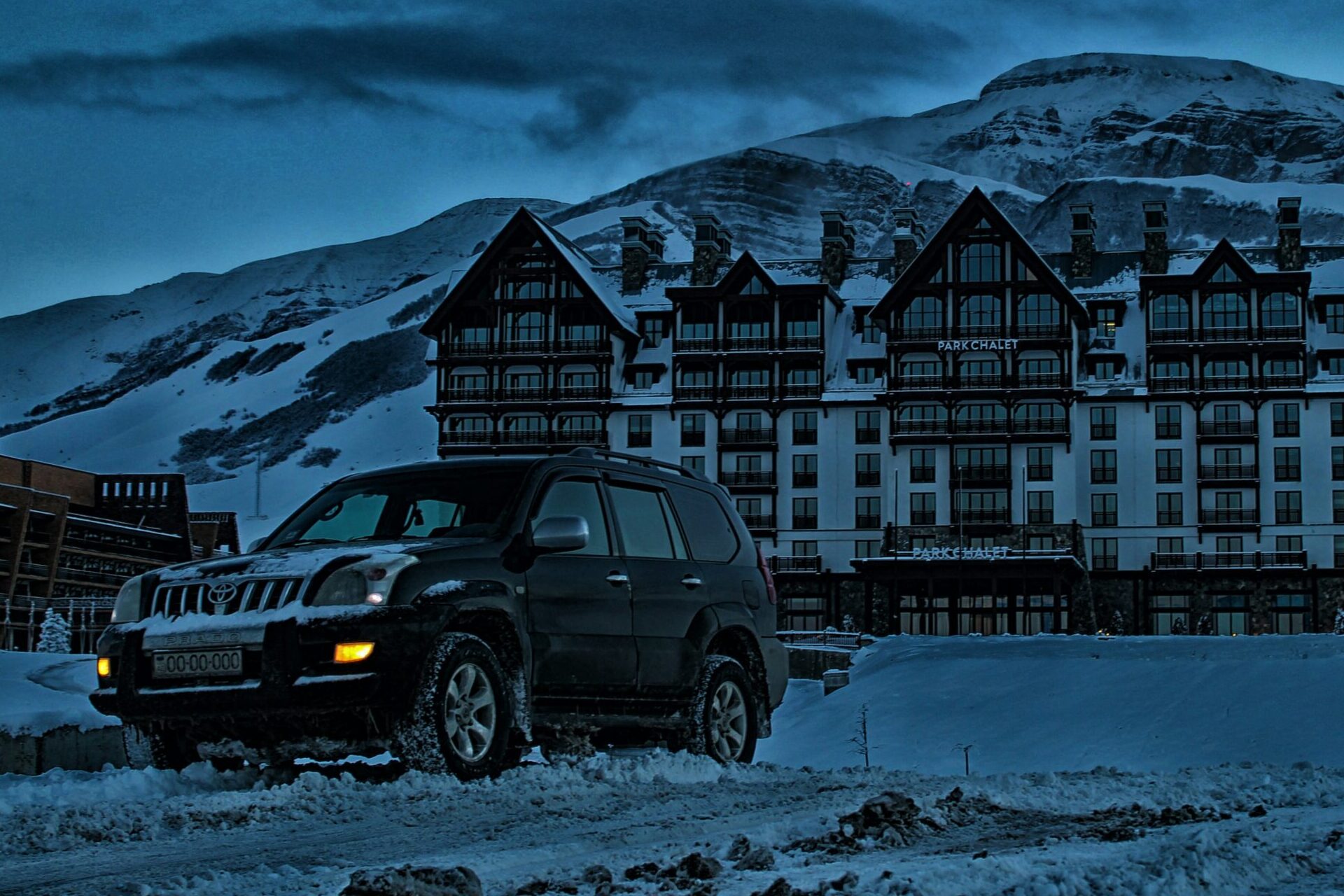 suv outside snowy building after sun has set.