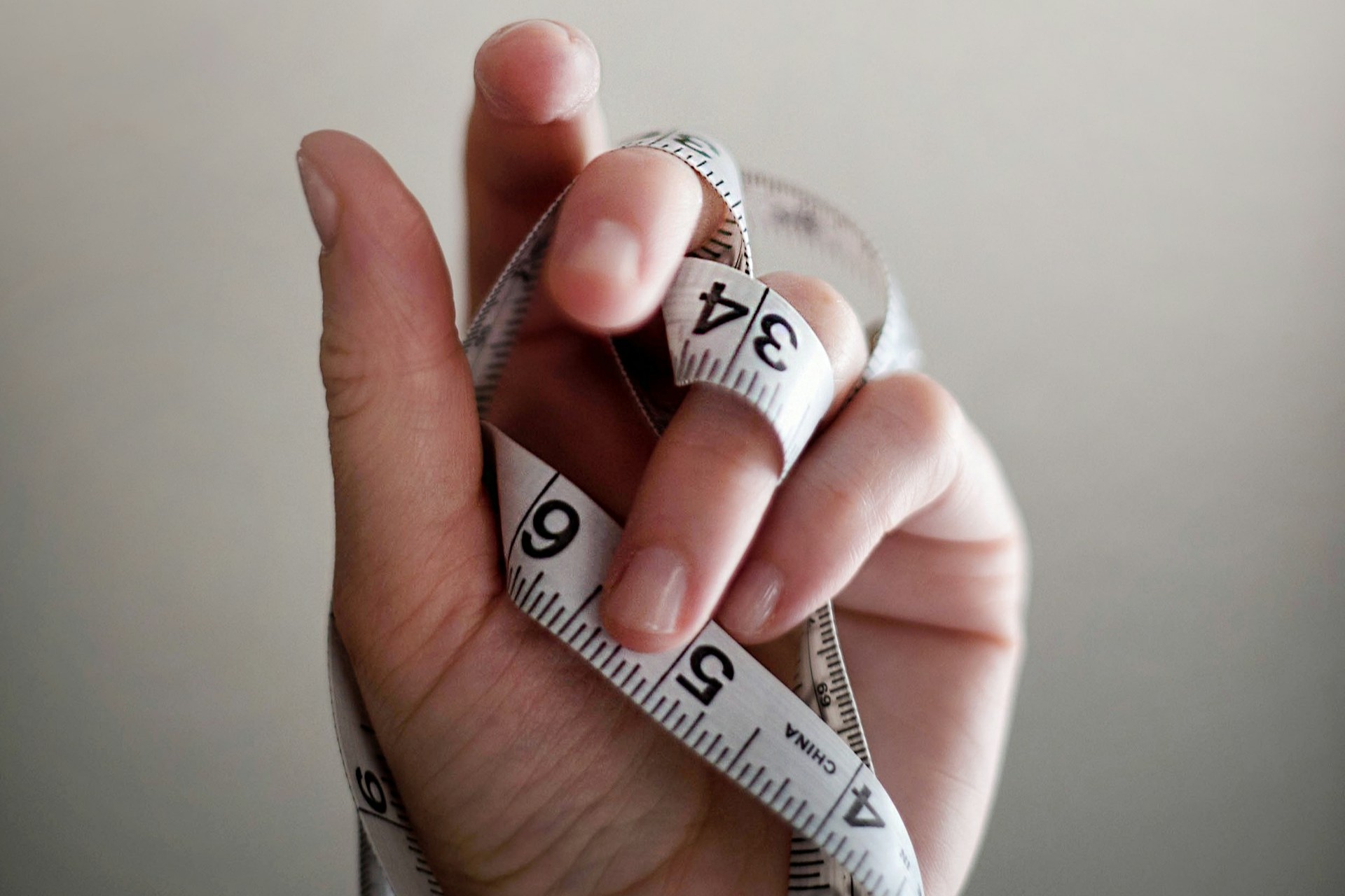 Person's left hand wrapped by tape measure.