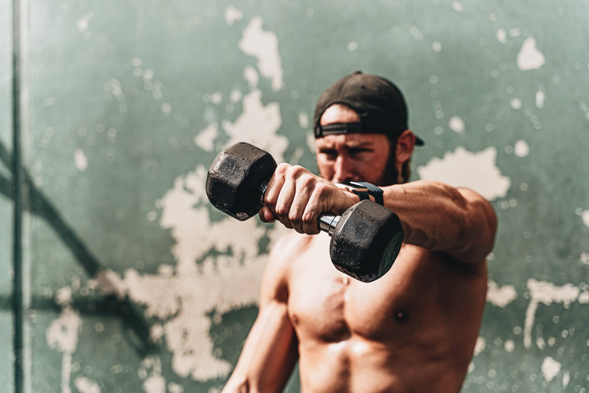 Shirtless man lifts a singular dumbbell with his left hand.