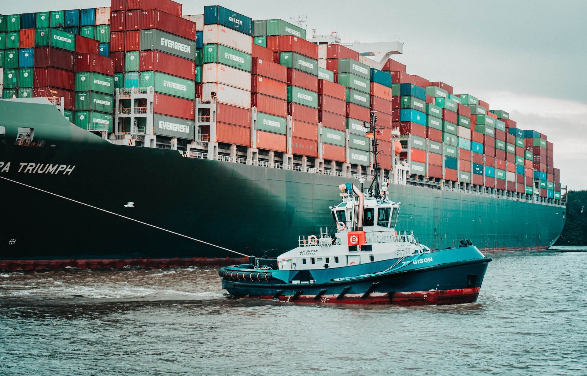 A small boat leads a cargo ship through a canal.