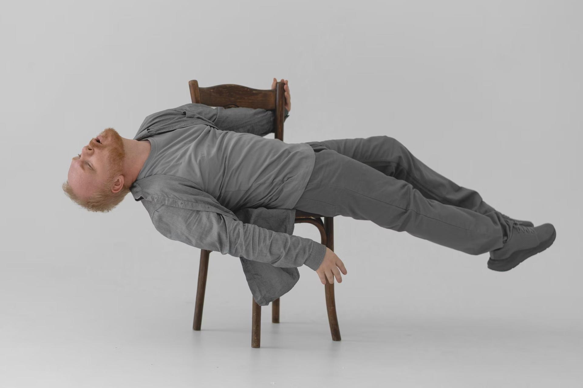 man in gray clothes lying across a chair
