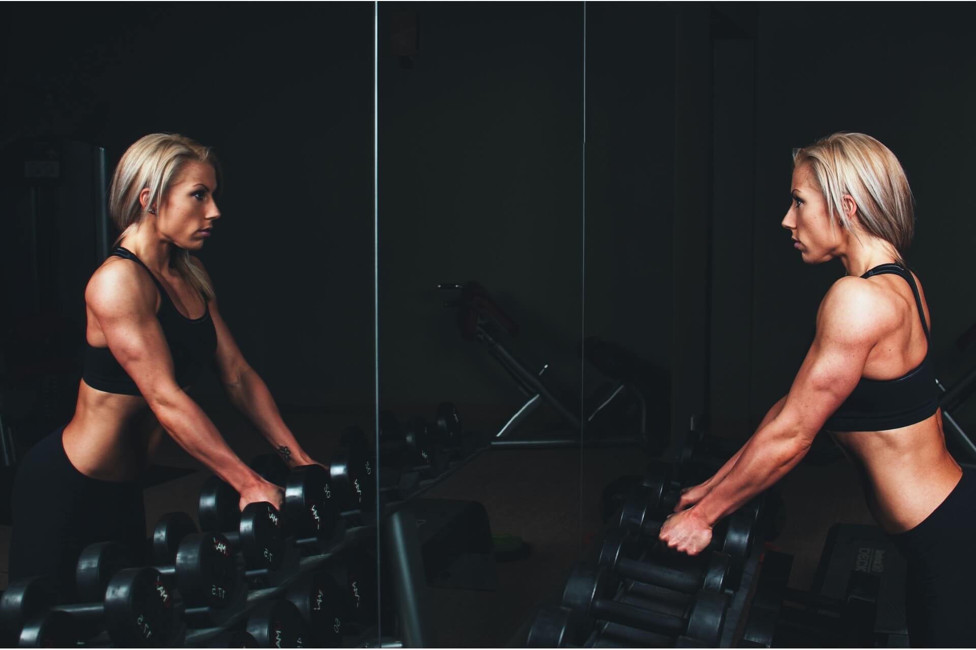 A woman looking at your reflection in the mirror while holding dumbbells