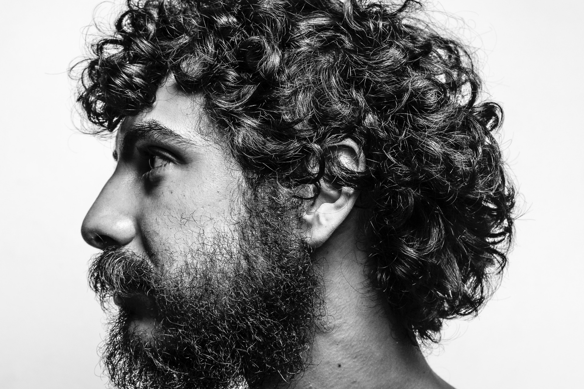 Side profile of a bearded man with a curly modern mullet hair style