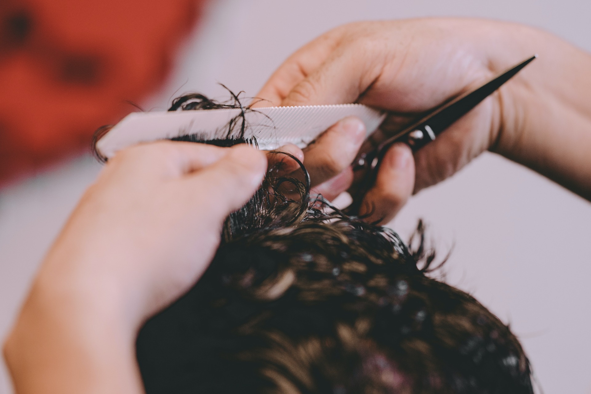 A barber's hands cutting a man's medium-length hair.