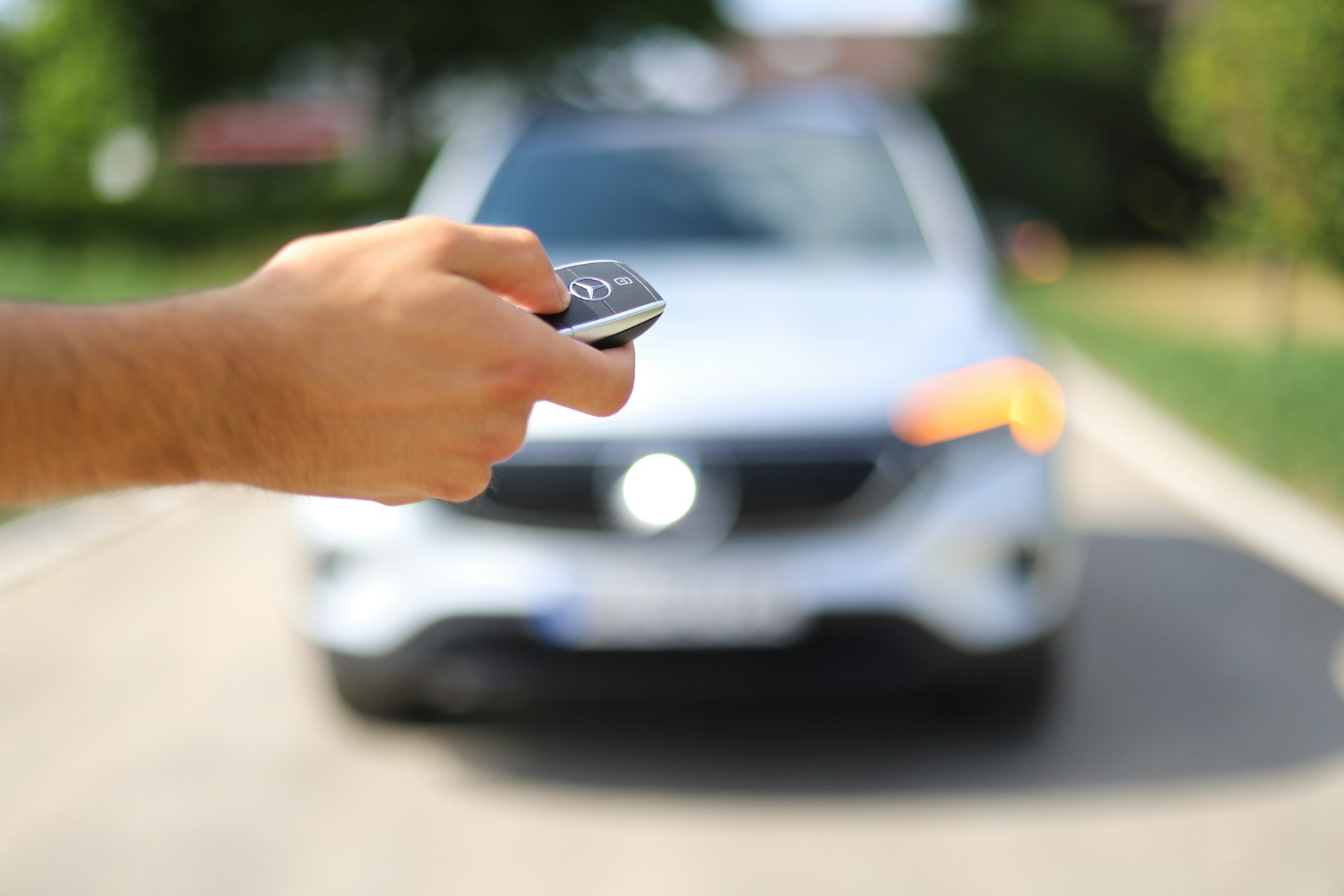 A person pressing a car key with a car in the background