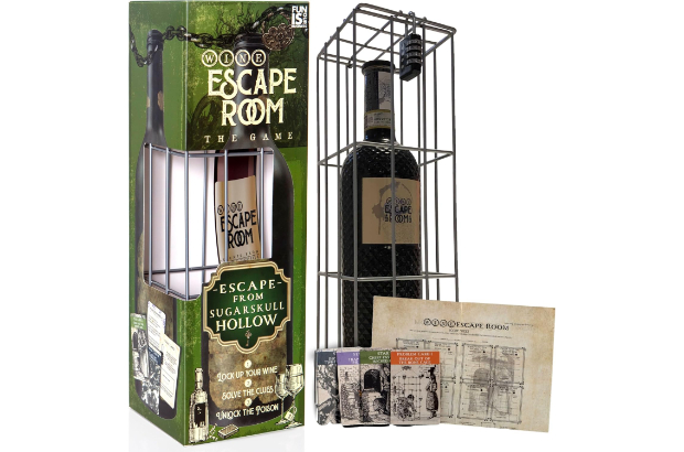 A bottle of wine in a green box with a couple of cards on a wooden table.