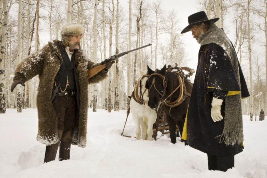 two men in the snow with warm coats and a gun