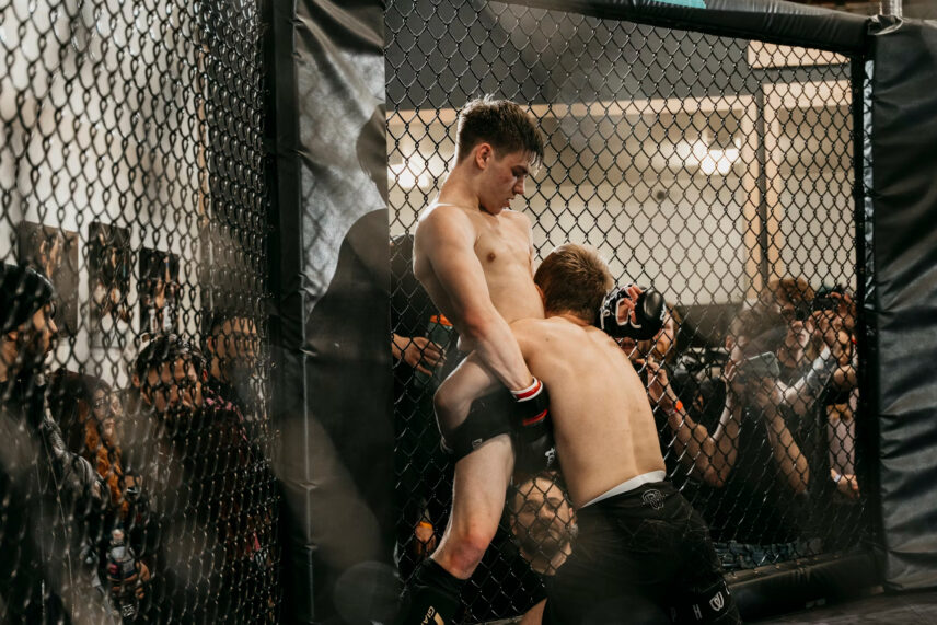 man pushing and lifting another man against a cage