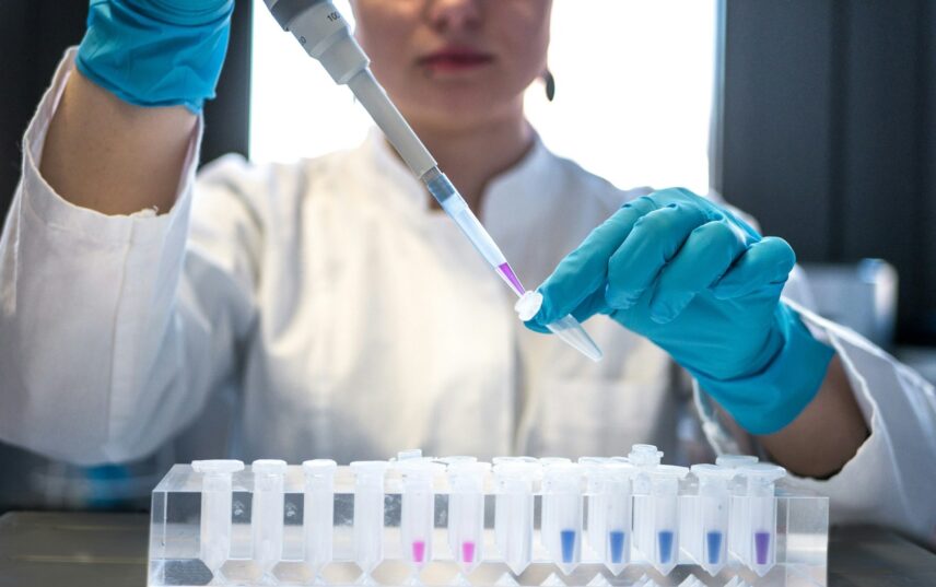 A woman in a lab coat stands holding a test tube, engaged in laboratory research or experimentation