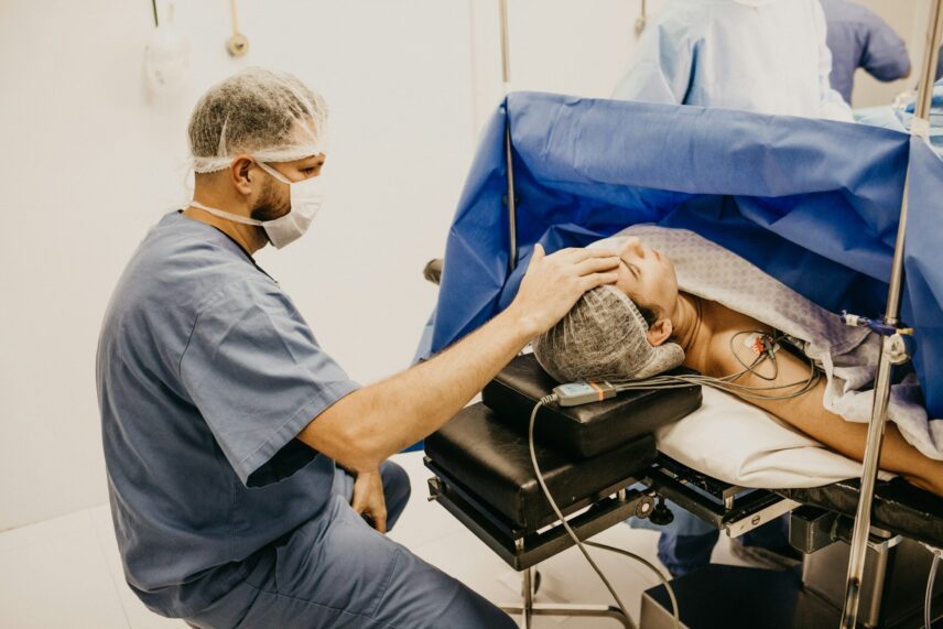 A doctor in scrubs and a mask gently holds a patient's head on an operating table, conveying care and reassurance in a medical setting