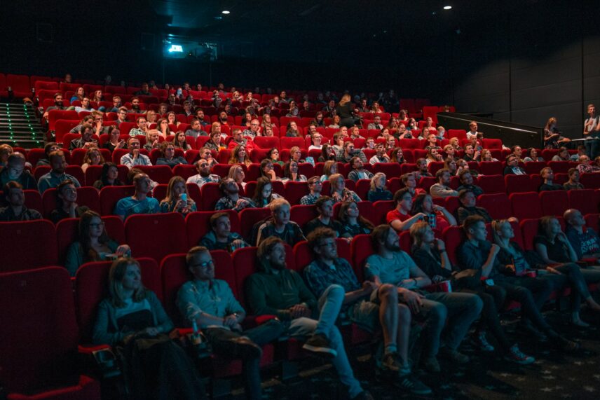 A large audience is seated in a theater with classic red cinema seats, attentively watching a movie .