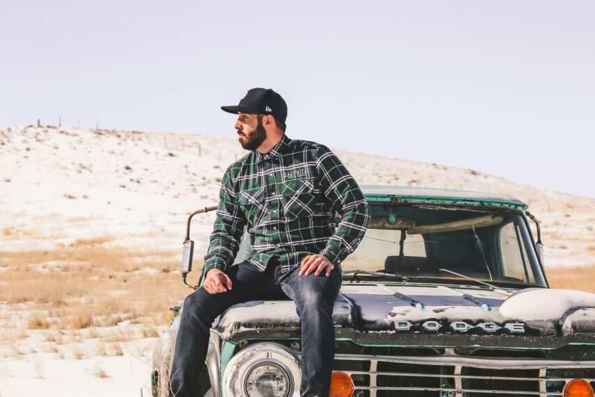 A man sitting on a car wearing a flannel shirt