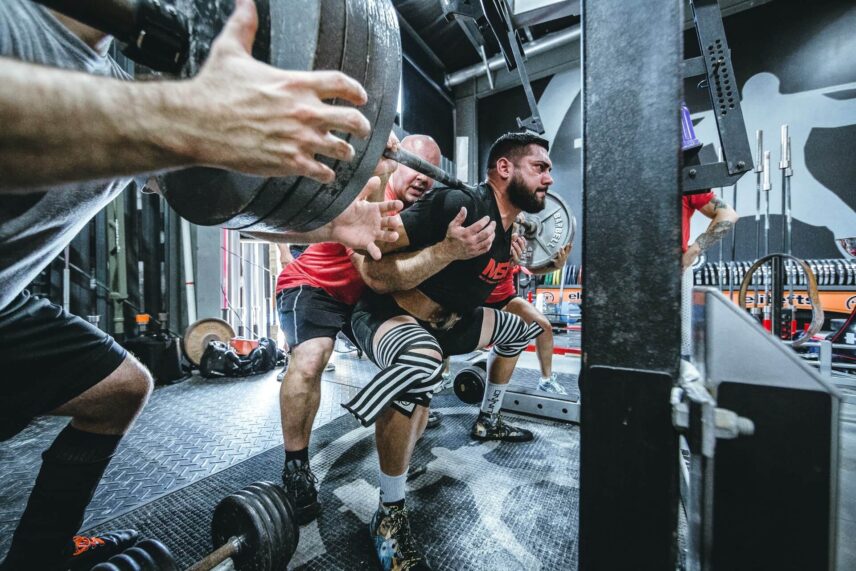 Man squatting on a bench with a spotter behind him