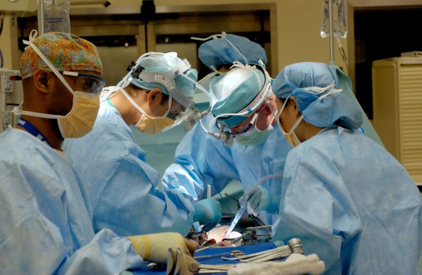 A team of surgeons in blue scrubs performs surgery under bright lights in an operating room. Focused expressions convey precision and teamwork.