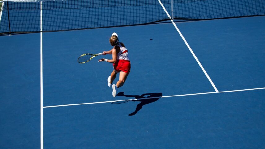 A tennis player in mid-air, preparing to hit the ball on a blue court.