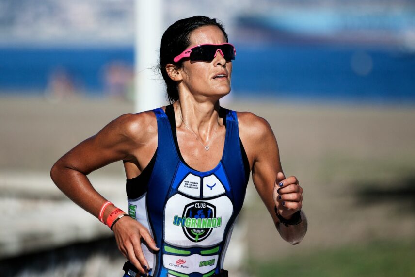 A woman dressed in a triathlon suit jogs on the shoreline, with the sea and sky in the background.