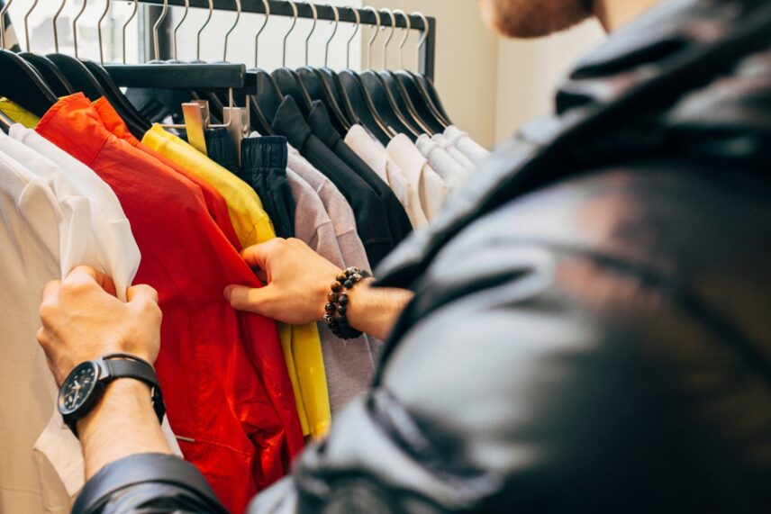 A man stands in front of a shirt rack, thoughtfully browsing through the selection of clothing.