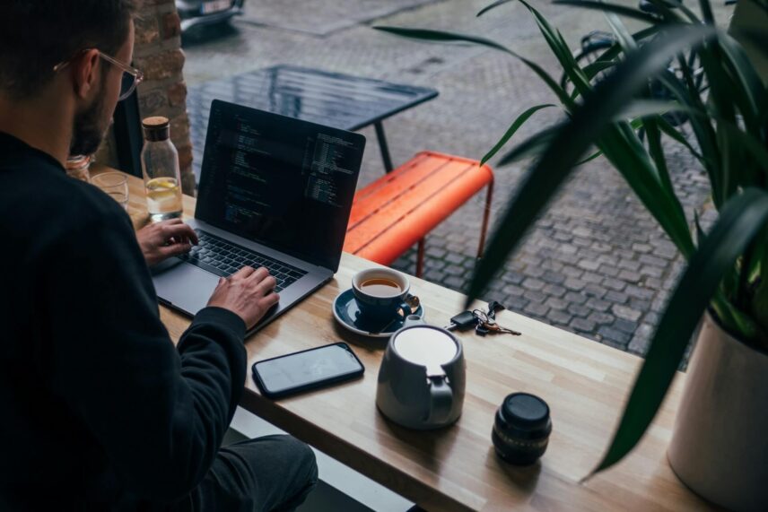 Man working on a MacBook with a smartphone at a coffee bar table