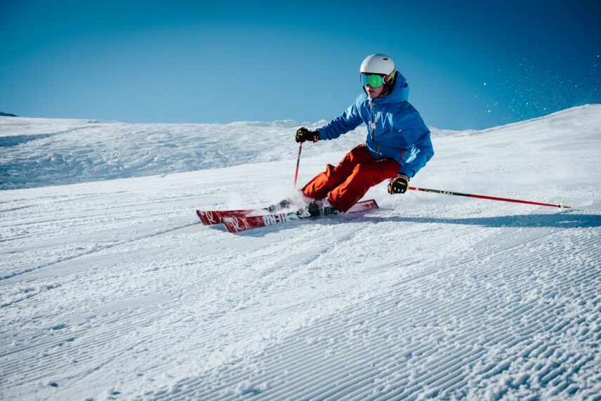 Skier in blue jacket and orange pants gracefully navigates a snowy slope under a clear blue sky, capturing the thrill and focus of winter sports.