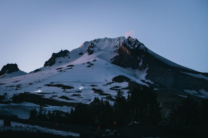 Snow-covered mountain against a twilight sky, with dark foreground trees. The serene scene conveys peacefulness and the beauty of nature.