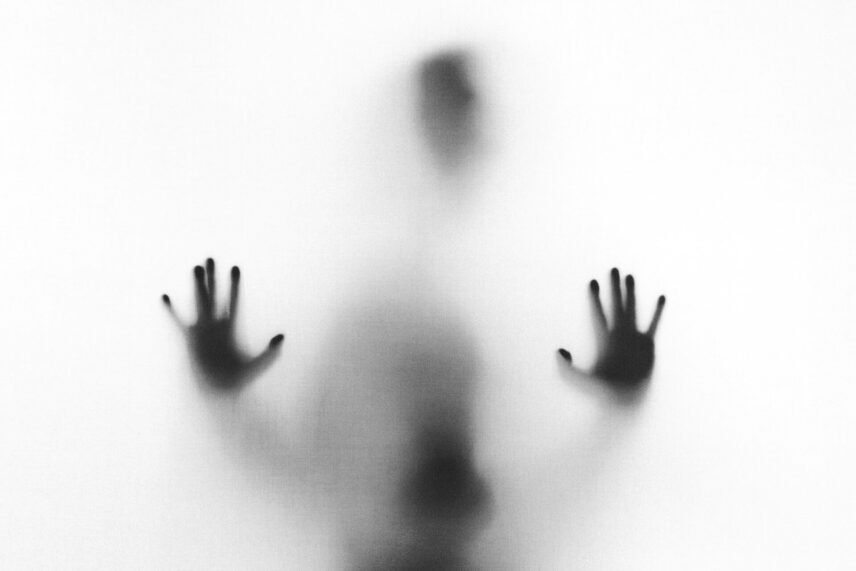 Silhouetted person with a hand pressed against fogged glass, creating an eerie, ghost-like effect