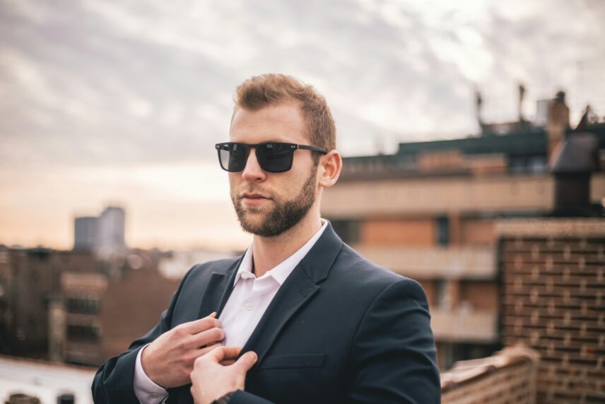 A well-dressed man in sunglasses is adjusting his outfit, showcasing a polished and sophisticated appearance.