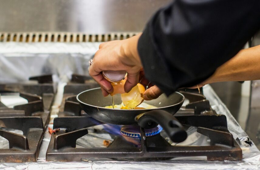 An individual cooking on a stove, cracking an egg on a pan.