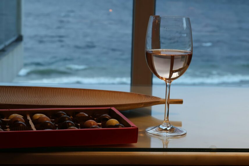 Wine glass with pink wine next to box of chocolates overlooking the sea for candy and alcohol pairing