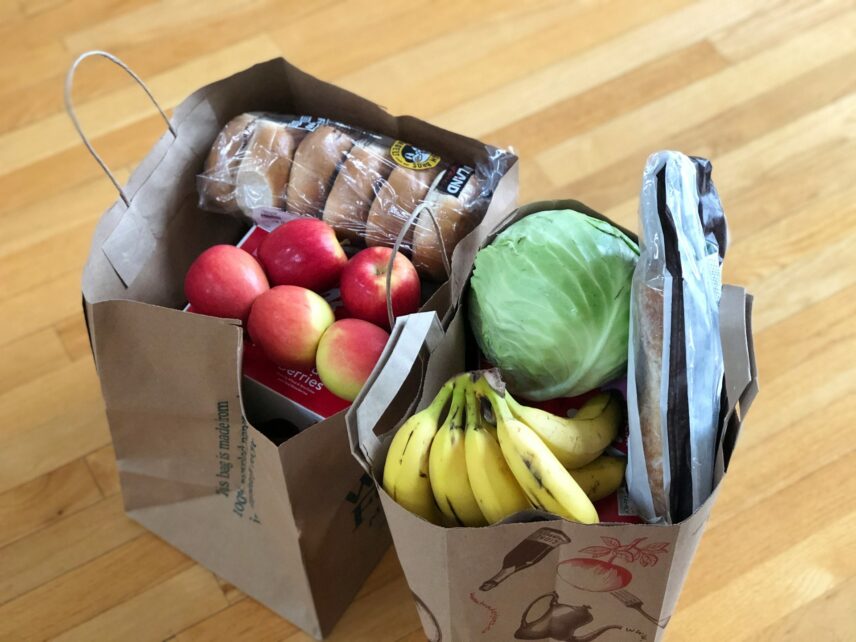 Two paper grocery bags full of produce, like lettuce, bananas, apples and bagels