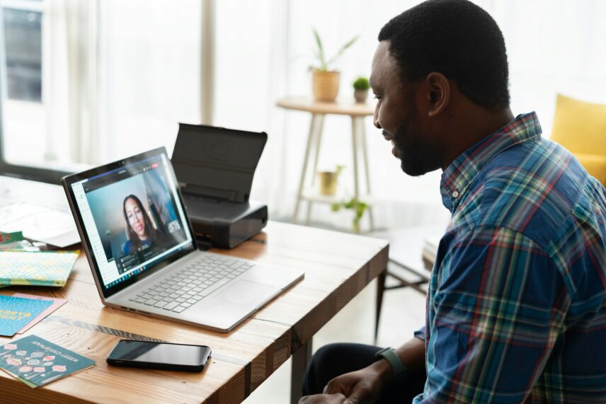 A man sits in front of a laptop on a desk while on a video call with a woman on the screen