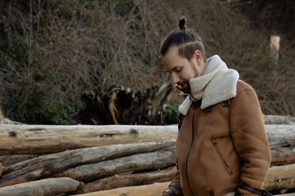 Man in coat next to logs.