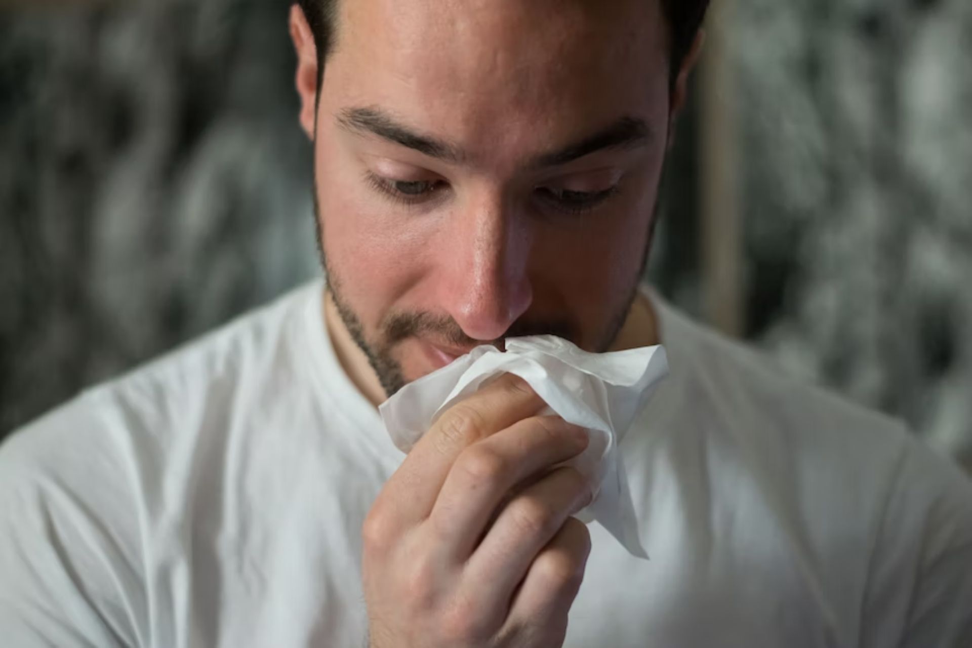 Man dealing with allergies, using tissue.