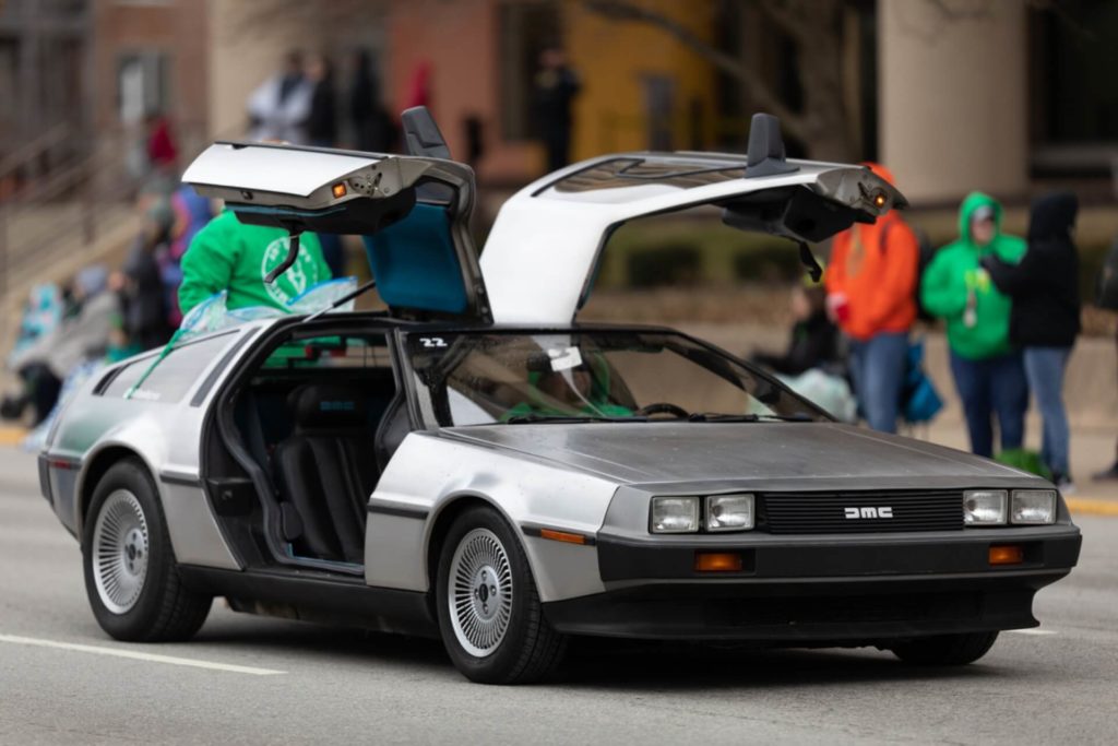 A DeLorean car on the street with the doors open. 