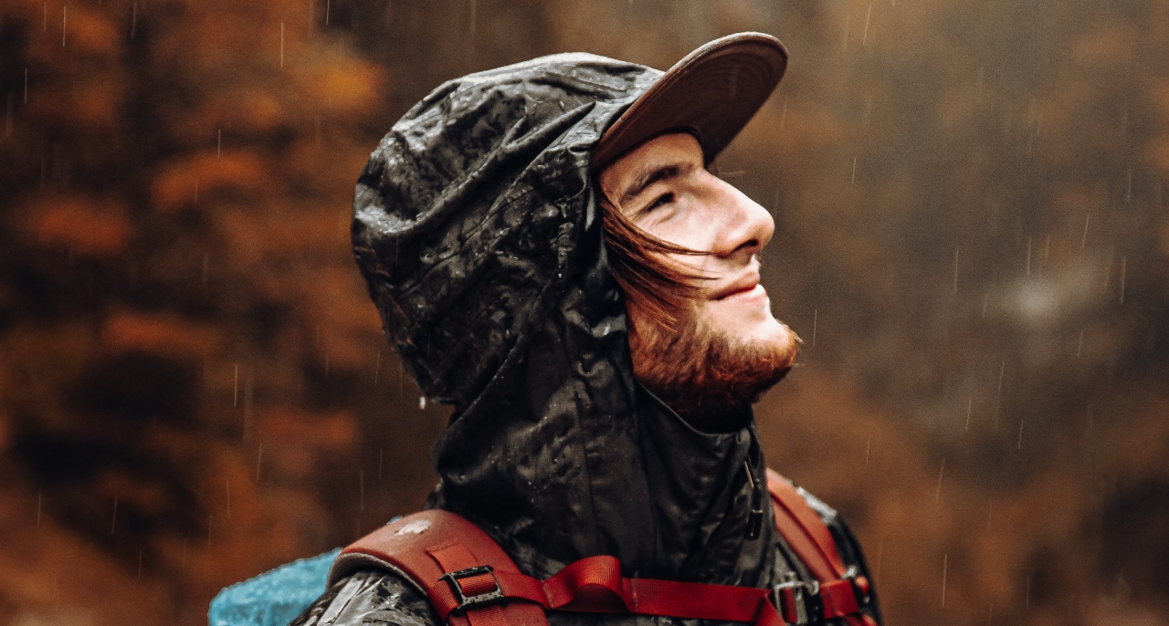 A man wearing waterproof gear looking up at rainy weather.