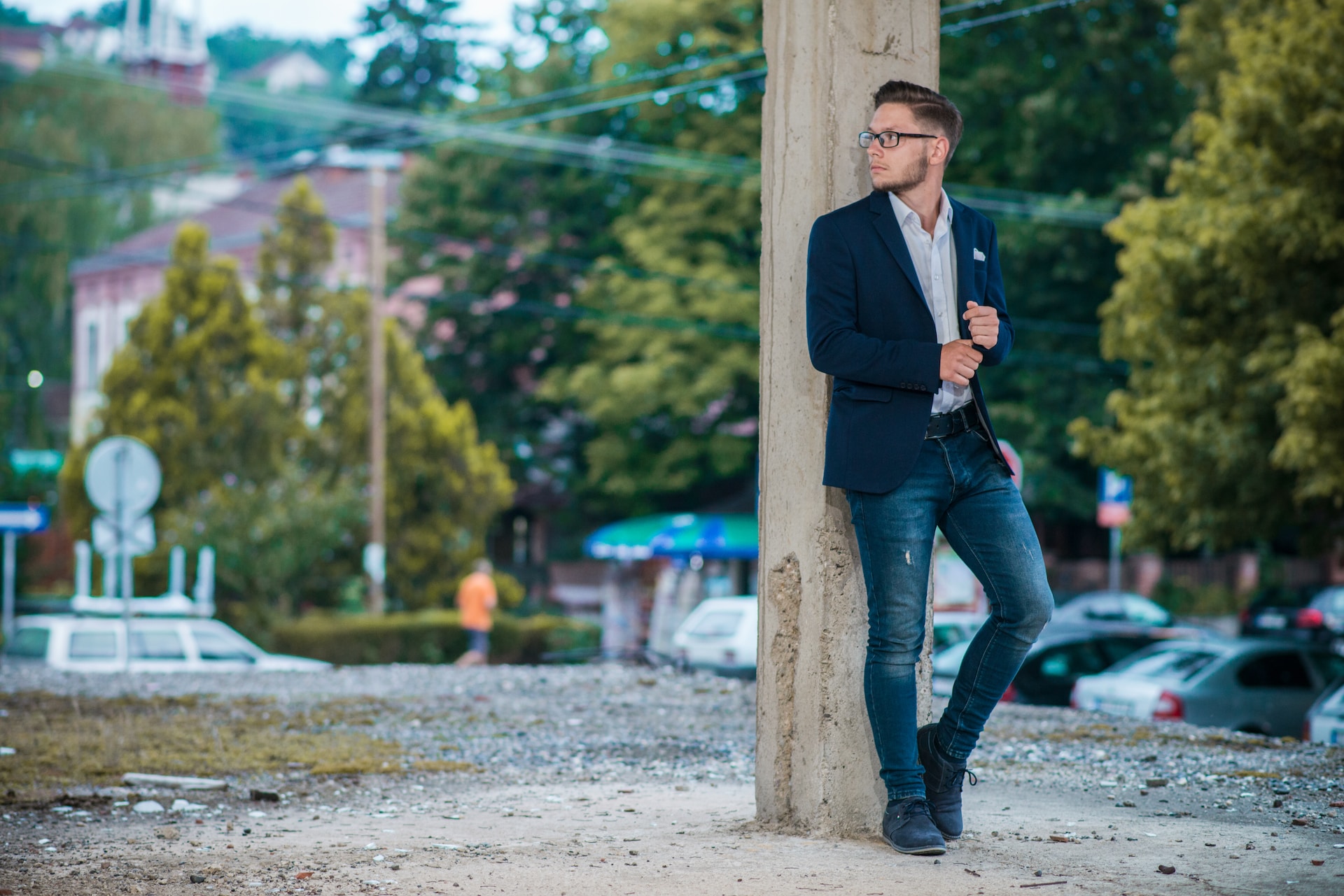 Man in suit jacket and jeans leaning against wood pole.