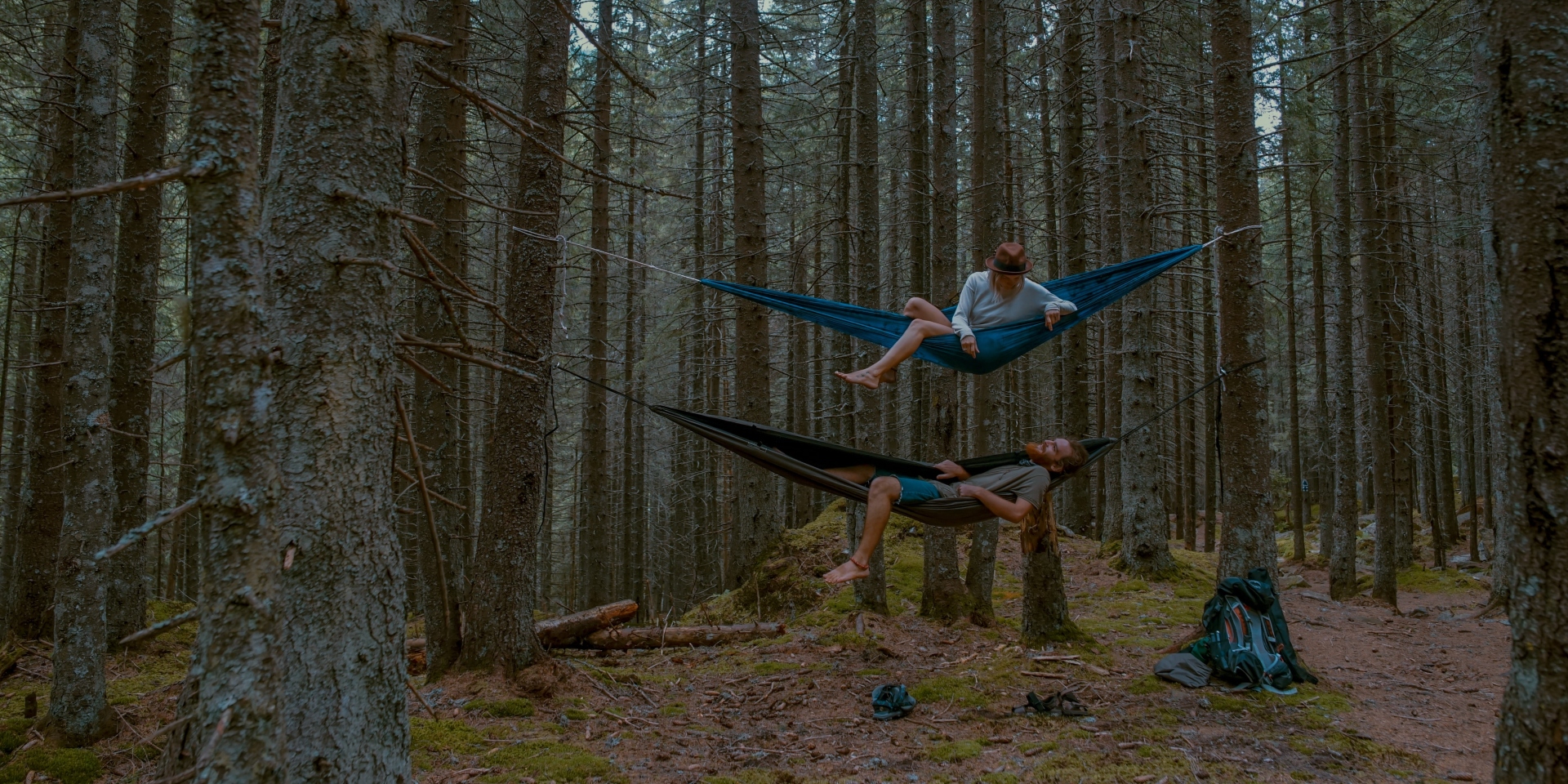 A man and a woman in two vertically stacked hammocks in the forest who know how to relax in nature
