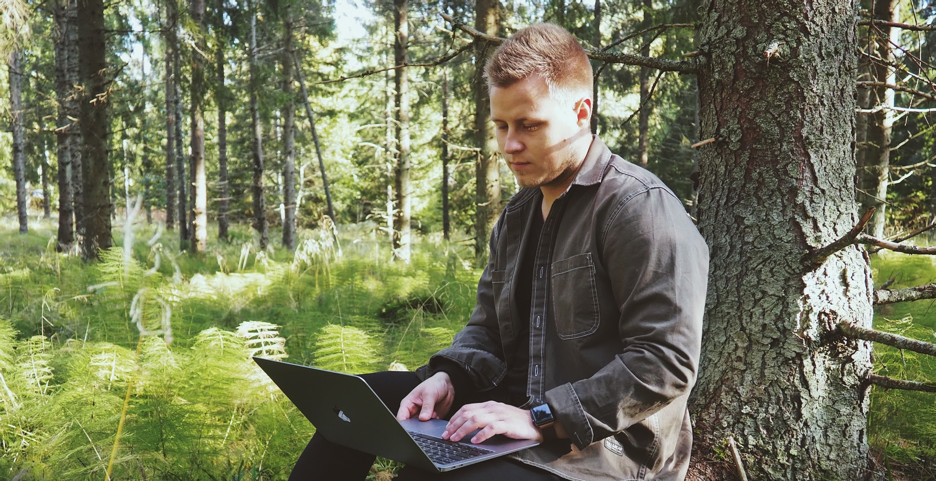 A man looking at a laptop in the woods
