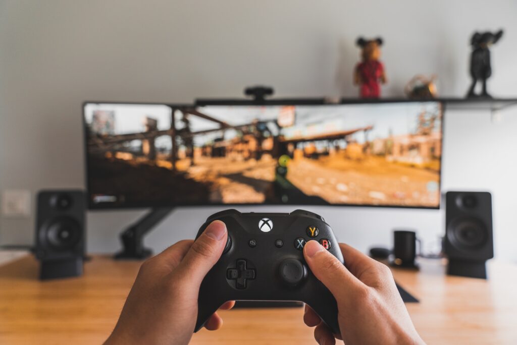 XBox controller and hands in front of large game screen.