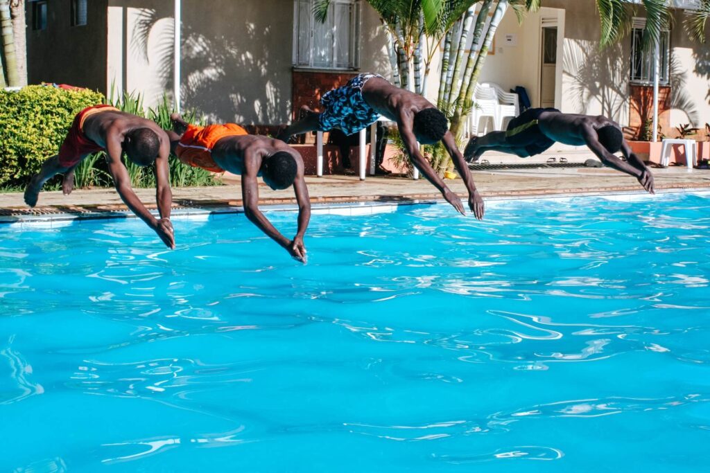 Four guys diving headfirst into a swimming pool. 