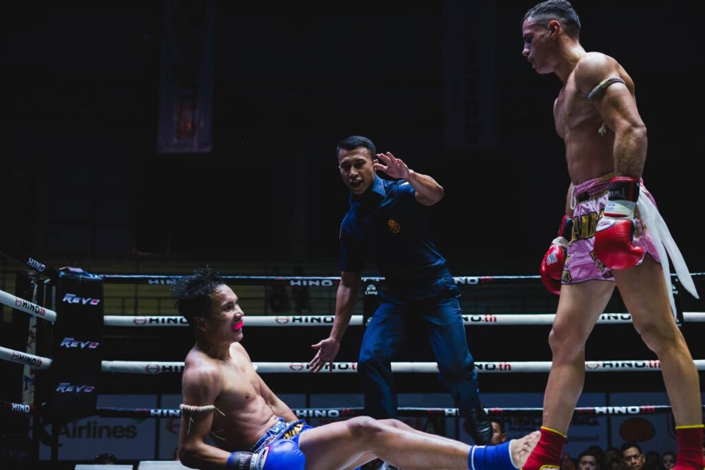 Muay Thai fighter standing after knocking down his opponent while the referee counts