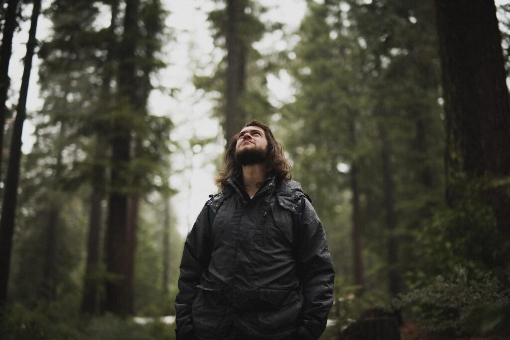 Man with long hair looks at the sky while walking in the forest