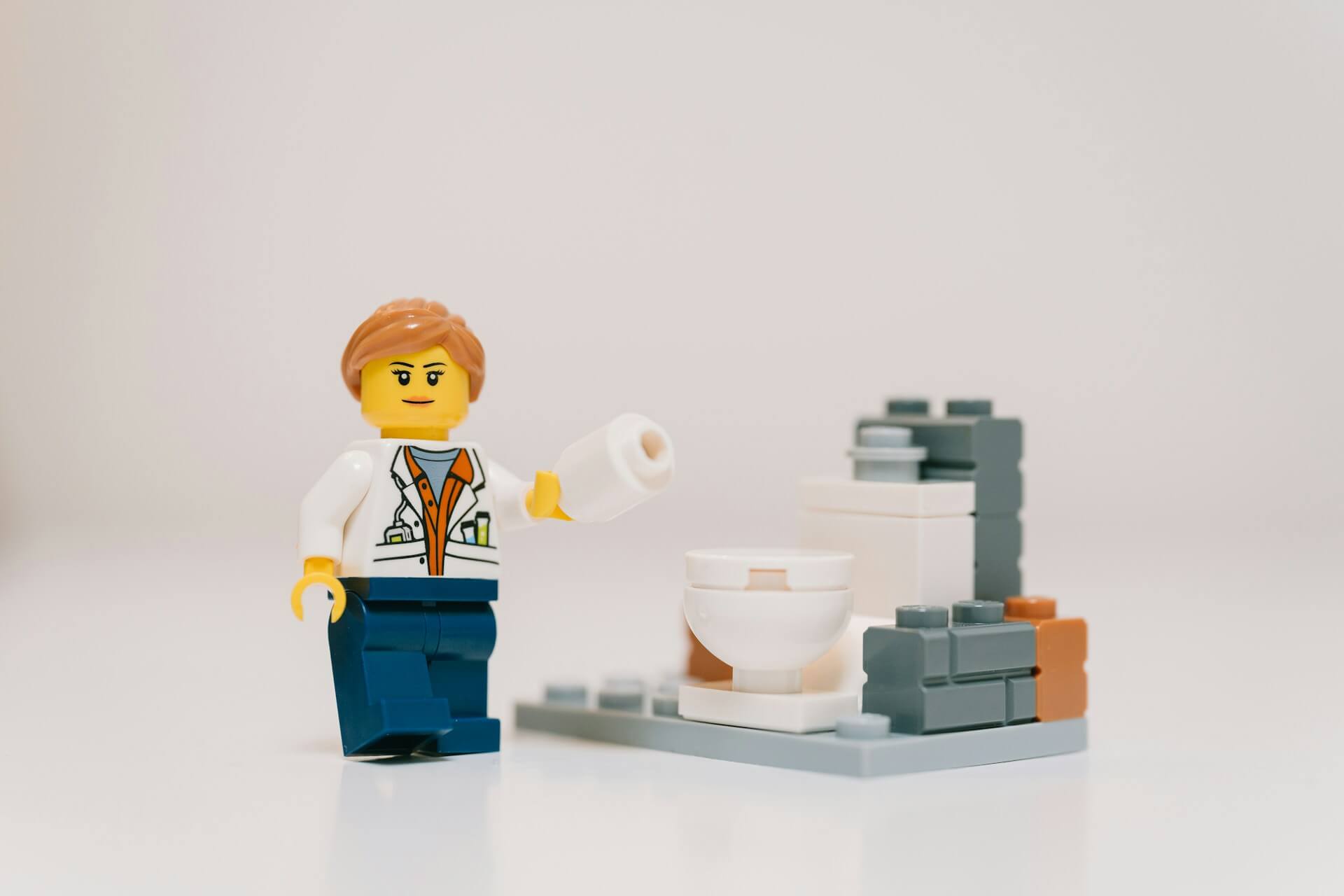 Lego handyman holding toilet paper next to a toilet
